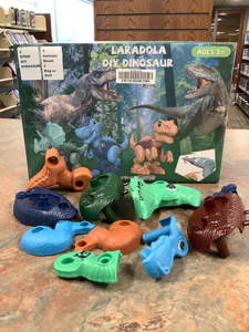 Photo of DIY Dinosaur STEM Kit with blue, green, and brown kit pieces laid out in front of the box.