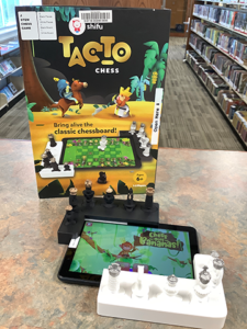Photo of the Tacto Chess STEM Kit contents: a tablet, black and white tablet frames, and chess figurines laid out in front of the box.