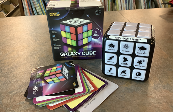 Photo of the Galaxy Cube, a ring of game cards, and it's box on top of a bookshelf.