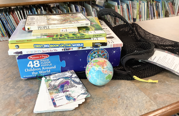 Photo of the contents of the Geography Theme Kit, which includes a DVD, four books, a puzzle, small squishy globe, and flash card deck. 