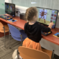 A child is kneeling on a small chair and touching the screen of an AWE learning computer.