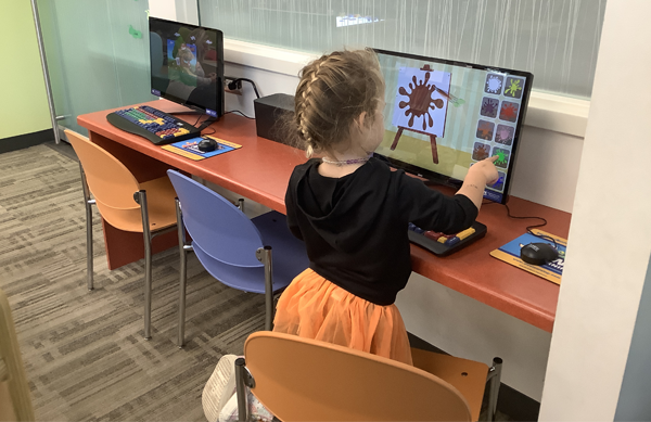 A child is kneeling on a small chair and touching the screen of an AWE learning computer. 