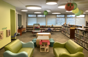 Photo of the Play Spot area in the Library, with two small couches, a dollhouse, light table, and two small tables with chairs.