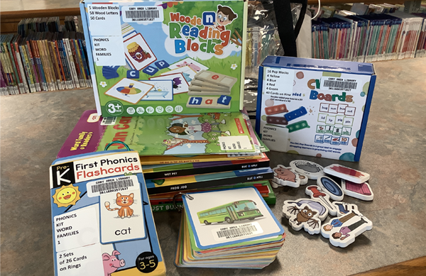 Photo of the contents of the Word Families Kit 1. There are a stack of reader books, flashcards, cardboard shapes, and a box of reading blocks.